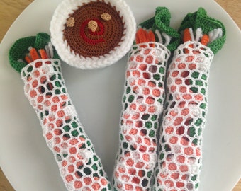 May include: Three crocheted spring rolls with green and orange details, and a crocheted bowl of brown sauce.