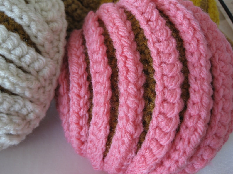 May include: Two crocheted balls, one white with brown stripes and one pink with brown stripes.