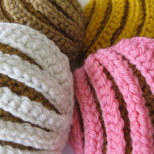 May include: Three crocheted striped balls in brown, white, yellow, and pink. The balls are made with a textured yarn and have a striped pattern.