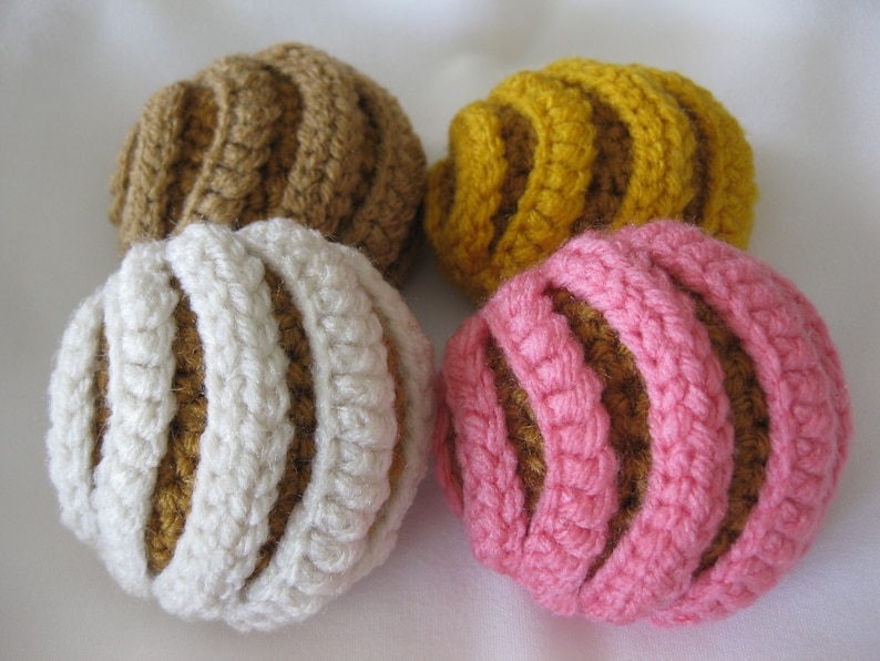 May include: Four crocheted balls in different colors: brown, yellow, white, and pink. Each ball has a striped pattern.