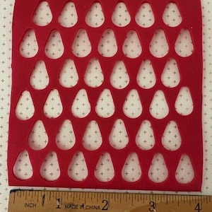 May include: A red felt sheet with 36 teardrop-shaped cutouts, each filled with a white teardrop shape adorned with small gray crosses. A wooden ruler with inch measurements is at the bottom.