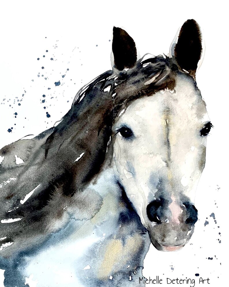 May include: Watercolour painting of a white horse with a black mane and tail. The horse is looking directly at the viewer with a soft expression. The background is a light blue with white splatters.