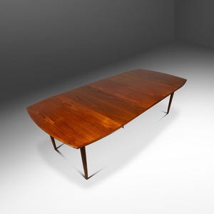 May include: A mid-century modern dining table with a rich, warm wood finish. The table has a rectangular top with gently curved ends and slender, tapered legs. The table's dimensions are approximately 72 inches long and 36 inches wide.