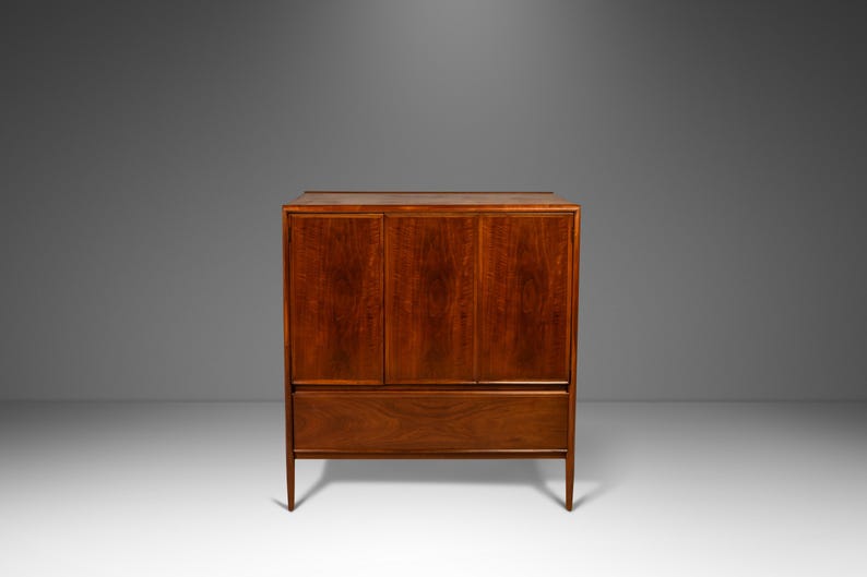 May include: A mid-century modern cabinet with three doors and a drawer. The cabinet is made of wood and has a rich brown finish.