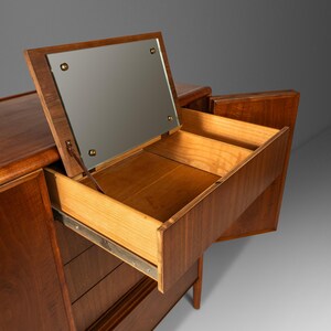May include: A mid-century modern walnut dresser with a mirrored top and three drawers. The dresser has a warm brown finish and is in good condition.