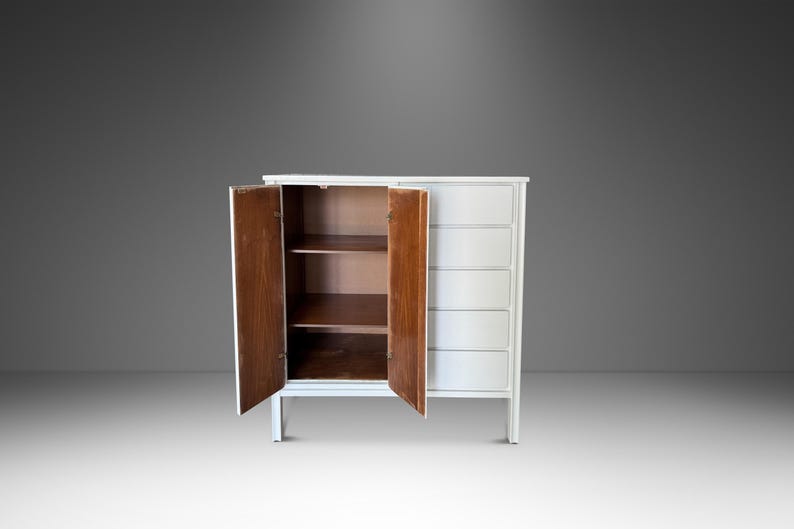 May include: A white cabinet with two doors open, revealing shelves. The cabinet has a series of drawers on the right side. The doors and interior shelves are a warm brown color, contrasting with the white exterior.