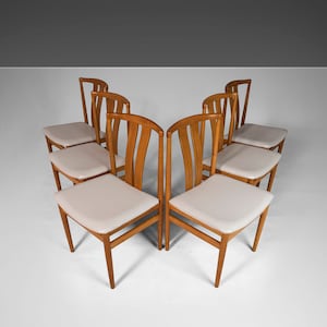 May include: Six wooden dining chairs with white upholstery. The chairs are arranged in a circle, with the backs of the chairs facing outward.