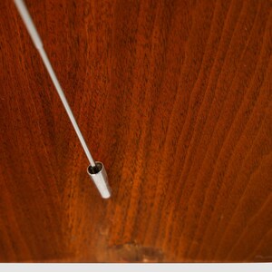 May include: A close-up of a silver metal rod with a hollow end, resting on a dark brown wooden surface.