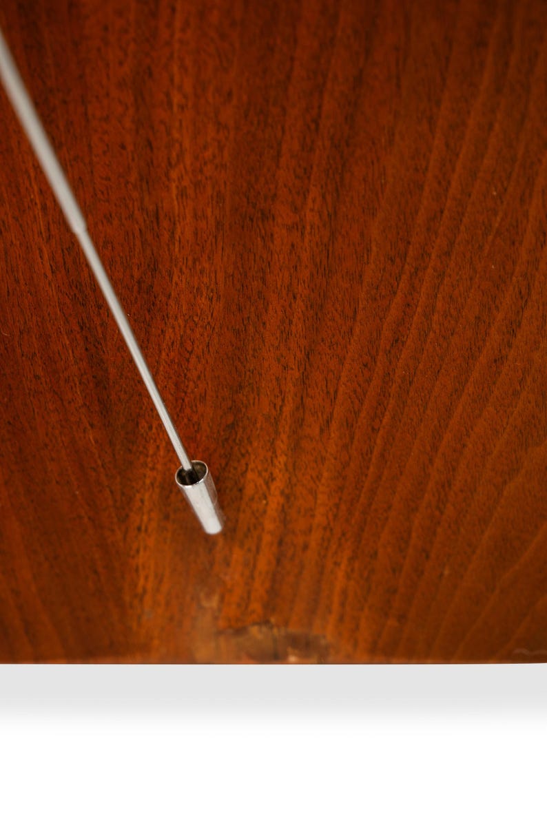 May include: A close-up of a silver metal rod with a hollow end, resting on a dark brown wooden surface.