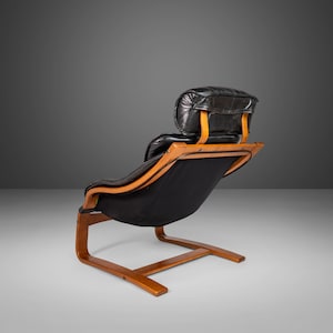May include: A black leather lounge chair with a wooden frame and a curved back. The chair has a headrest and a low profile.