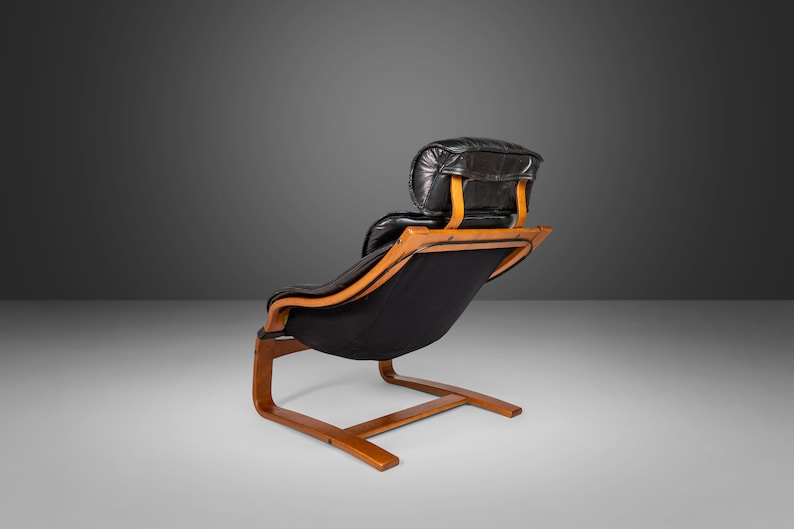 May include: A black leather lounge chair with a wooden frame and a curved back. The chair has a headrest and a low profile.