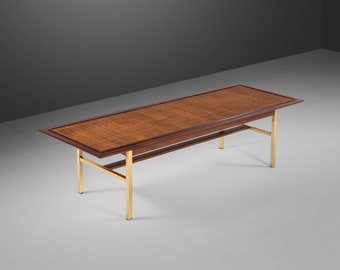 May include: A long, rectangular coffee table with a woven wood top and a brass frame. The table has a simple, mid-century modern design.