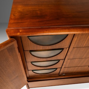 May include: A vintage wooden dresser with six drawers and a cabinet door. The drawers have curved glass fronts and the cabinet door is open.