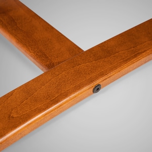 May include: Close-up of a wooden frame with a dark brown stain. The frame has a smooth finish and a small black screw in the lower right corner.