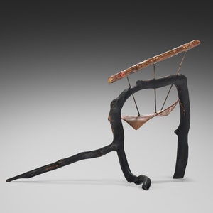 May include: A black metal sculpture with a copper hammock hanging from a branch. The sculpture is abstract and organic in form.