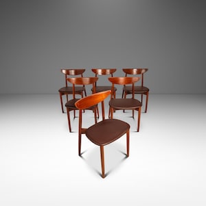 May include: A set of seven wooden chairs with curved backs and brown seats. The chairs are arranged in a group, with one chair positioned in front. The wood has a warm, reddish-brown tone.