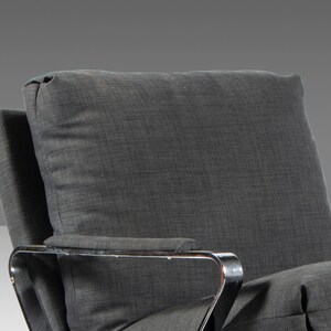 May include: A gray upholstered armchair with a chrome frame. The chair has a high back and a wide seat. The upholstery is a textured fabric with a subtle pattern.