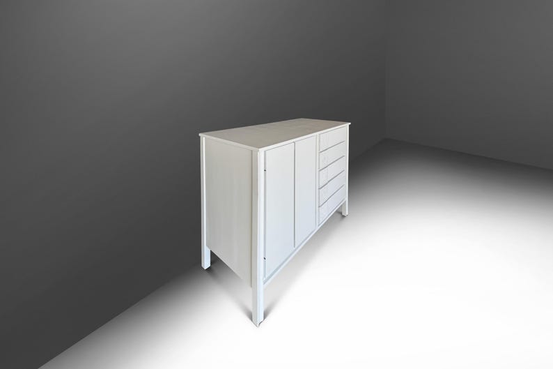 May include: A white wooden cabinet with a rectangular top, two doors, and four drawers. The cabinet has a simple, modern design with clean lines and a light finish. The cabinet is set against a gray background.