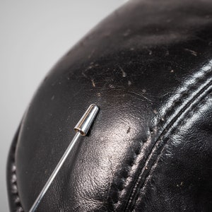 May include: Close-up of a black leather surface with a silver pin sticking into it.