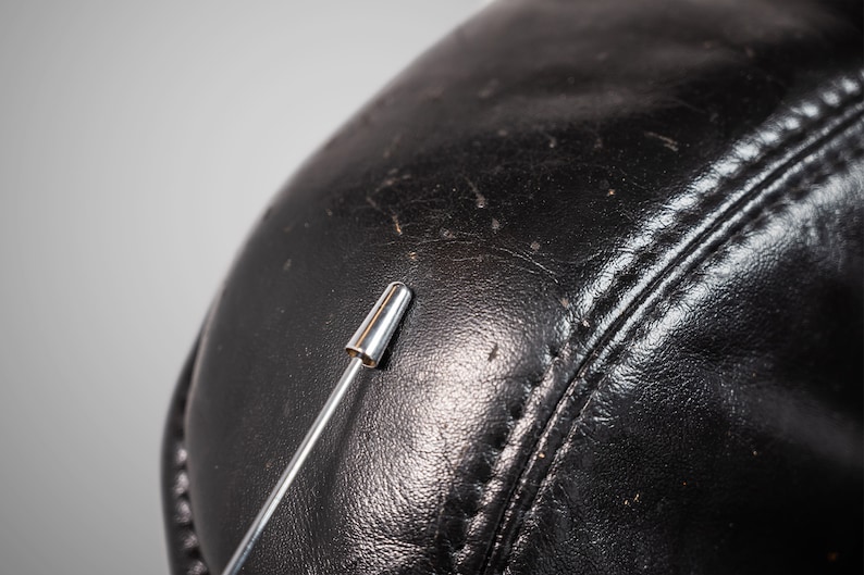 May include: Close-up of a black leather surface with a silver pin sticking into it.