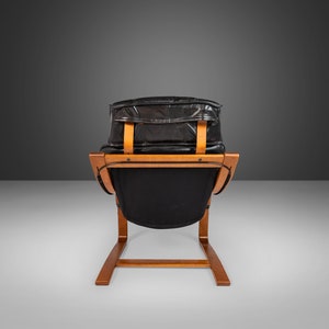 May include: A black leather armchair with a wooden frame. The chair has a curved back and a low seat. The chair is in a minimalist style.