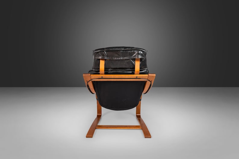 May include: A black leather armchair with a wooden frame. The chair has a curved back and a low seat. The chair is in a minimalist style.