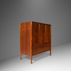 May include: A mid-century modern cabinet with a wood grain finish. The cabinet has two doors and a single drawer. The cabinet is made of solid wood and has a warm brown color.