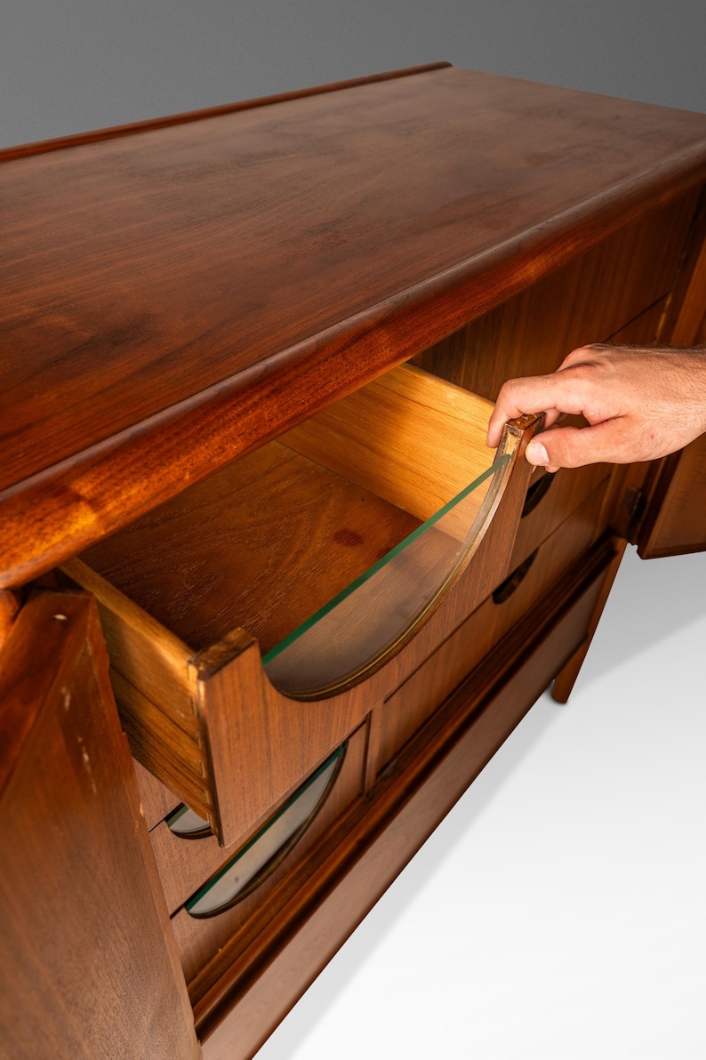 May include: A vintage wooden dresser with a curved design and glass-fronted drawers. The dresser has a rich brown finish and is in good condition.