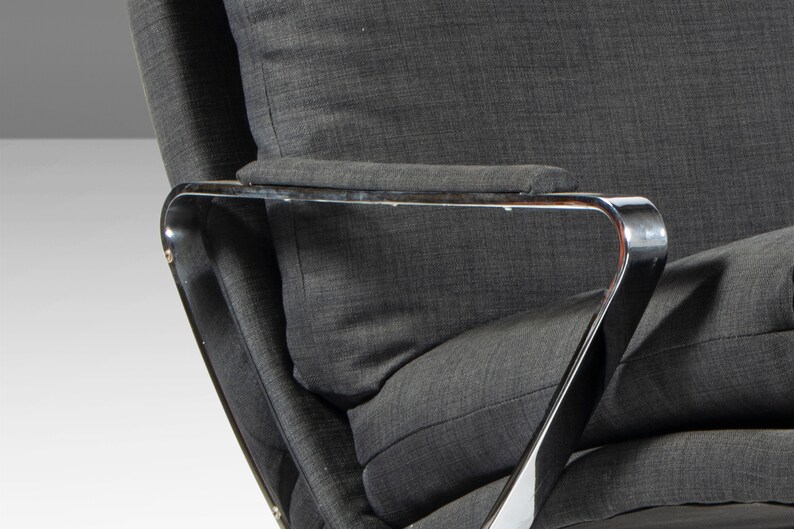 May include: Close-up of a gray fabric armchair with a chrome frame. The armrest is padded and the chair has a modern design.