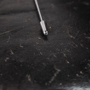 May include: Close-up of a silver metal antenna tip on a black leather surface.