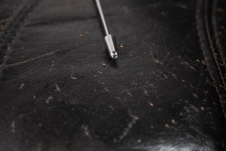 May include: Close-up of a silver metal antenna tip on a black leather surface.