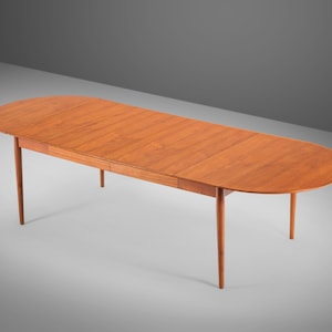 May include: A wooden oval-shaped dining table with a leaf extension. The table has a light brown finish and four slender legs.