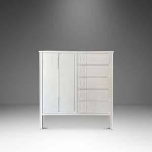 May include: A white cabinet with a door on the left and five drawers on the right. The cabinet has a simple, modern design with clean lines and a minimalist aesthetic. The drawers have decorative carved details.