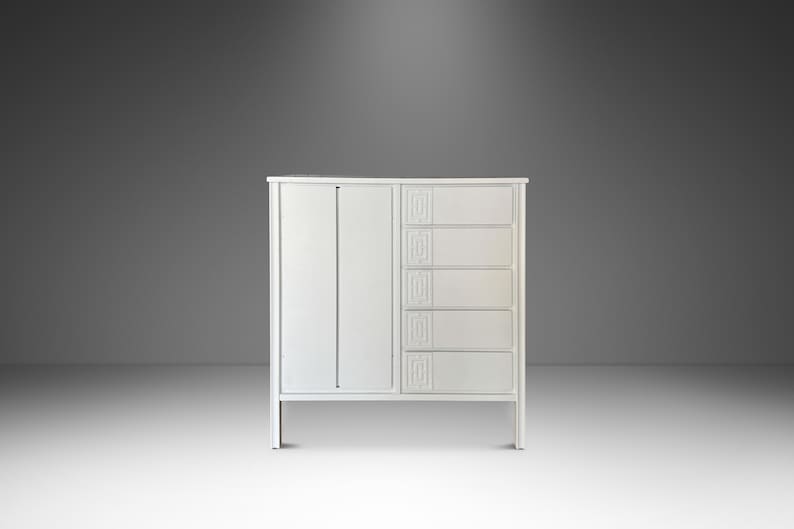 May include: A white cabinet with a door on the left and five drawers on the right. The cabinet has a simple, modern design with clean lines and a minimalist aesthetic. The drawers have decorative carved details.
