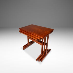 May include: A set of three nesting tables made of dark wood. The tables are stacked on top of each other, with the largest table on the bottom and the smallest table on top.