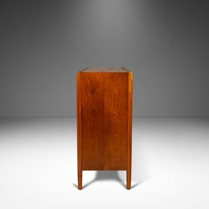May include: A mid-century modern wooden cabinet with a rich brown finish. The cabinet has a simple design with clean lines and a rectangular shape. It features four legs and a solid wood construction.
