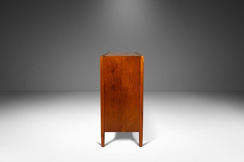 May include: A mid-century modern wooden cabinet with a rich brown finish. The cabinet has a simple design with clean lines and a rectangular shape. It features four legs and a solid wood construction.