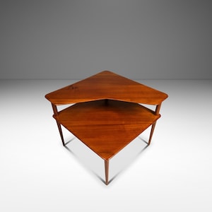 May include: A two-tiered, triangular wooden side table. The table has a rich, warm brown finish. The top tier is slightly larger than the bottom tier. The legs are slender and angled, providing support. The table is approximately 24 inches wide.
