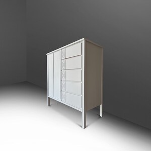 May include: A white cabinet with a vertical panel on the left and five drawers on the right. The drawers have decorative rectangular panels. The cabinet stands on four thin legs. The background is a gradient of gray.