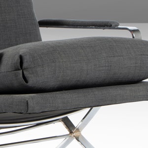 May include: A gray fabric armchair with a chrome frame. The chair has a thick, gray fabric cushion and a smaller, gray fabric pillow. The chair is angled slightly to the right.