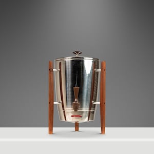 May include: A vintage chrome coffee percolator with wooden legs and handles. The coffee maker has a round lid with a small knob and a glass indicator. The wooden legs are a warm brown color.