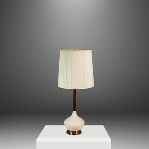 May include: A mid-century modern table lamp with a cream-colored, pleated lampshade. The lamp has a dark brown wooden stem and a white, rounded base. The lamp is approximately 28 inches tall.