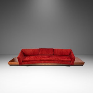 May include: A mid-century modern sofa with a vibrant red fabric. The sofa features a curved design and is set on a dark wood base with integrated side tables. The overall aesthetic is sleek and stylish.