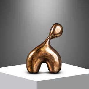 May include: A bronze abstract sculpture of a person with a rounded head and body. The sculpture is standing on a white pedestal.