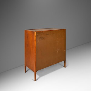 May include: A wooden cabinet with a light brown finish. The cabinet has four drawers and two doors. The back of the cabinet is visible, showing a label with the text "Danish Furniture Co. Inc. New York, N.Y."