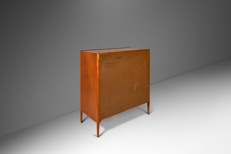 May include: A wooden cabinet with a light brown finish. The cabinet has four drawers and two doors. The back of the cabinet is visible, showing a label with the text "Danish Furniture Co. Inc. New York, N.Y."