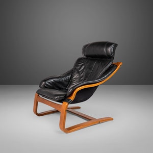 May include: A black leather armchair with a wooden frame and a curved base. The chair has a high back and a headrest.