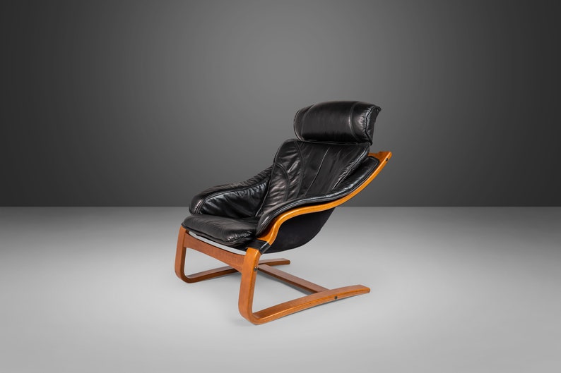 May include: A black leather armchair with a wooden frame and a curved base. The chair has a high back and a headrest.