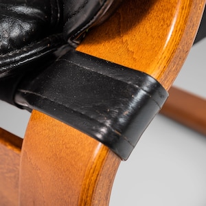 May include: Close-up of a wooden chair with black leather upholstery. The chair has a curved back and a simple design.