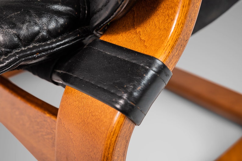 May include: Close-up of a wooden chair with black leather upholstery. The chair has a curved back and a simple design.